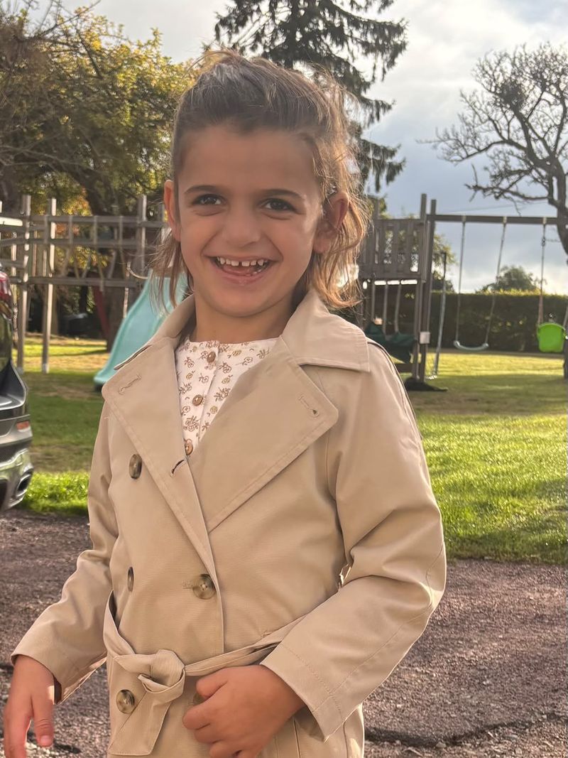 Alma souriante, en trench beige, dans le jardin